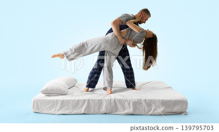 Man dipping woman backward on white bed from side view against blue background. Man dipping woman backward on white bed from side view against blue background. 139795703