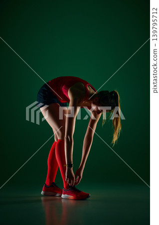Female athlete bending forward in post run stretch on green studio background Female athlete bending forward in post run stretch on green studio background 139795712