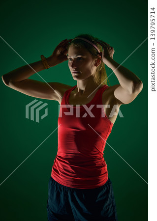 Focused female athlete adjusting headband before training on green background 139795714
