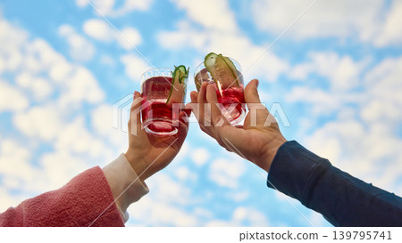 Red cucumber cocktails clinking against blue sky with copy space. Red cucumber cocktails clinking against blue sky with copy space. 139795741