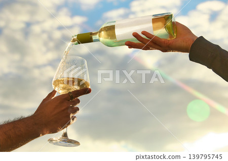 White wine pouring into glass against bright sky with sun flare White wine pouring into glass against bright sky with sun flare 139795745
