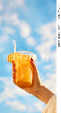 Orange iced drink in takeaway cup with blue sky copy space. Orange iced drink in takeaway cup with blue sky copy space. 139795748
