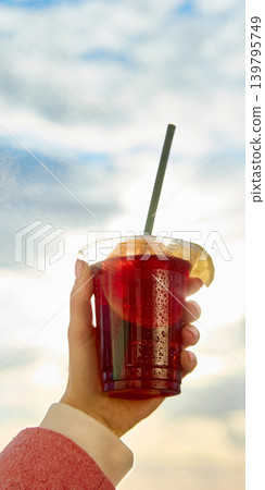 Close up of red iced drink with straw and citrus against bright sky. Close up of red iced drink with straw and citrus against bright sky. 139795749