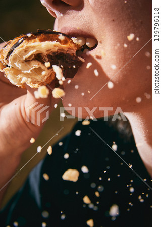 Teenager biting flaky croissant with falling crumbs in extreme food closeup. Teenager biting flaky croissant with falling crumbs in extreme food closeup. 139796118