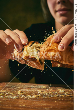 Hands breaking flaky croissant with flying crumbs in dramatic food closeup. Hands breaking flaky croissant with flying crumbs in dramatic food closeup. 139796121