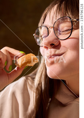 Young woman enjoying piece of bread with satisfied expression in closeup portrait Young woman enjoying piece of bread with satisfied expression in closeup portrait 139796128