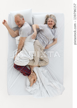 Smiling older couple lying in bed and playfully stealing blanket top view. 139796157