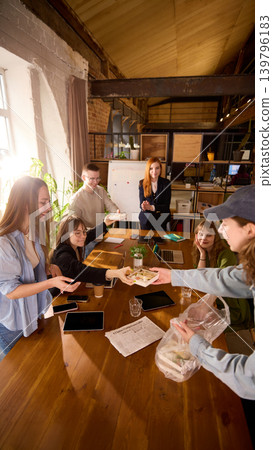 Food courier handing lunch box to office worker at meeting table. Food courier handing lunch box to office worker at meeting table. 139796183