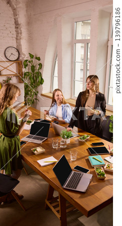 Women coworkers chatting while eating healthy lunch in bright office Women coworkers chatting while eating healthy lunch in bright office 139796186