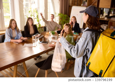 Food courier delivering lunch order to office team during meeting. Food courier delivering lunch order to office team during meeting. 139796199