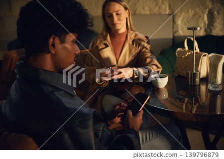 Couple using smartphones at lounge table with warm evening light. 139796879
