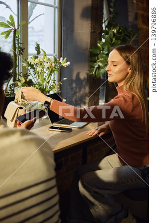 Woman making payment with smartwatch near laptop and handbag in stylish workspace Woman making payment with smartwatch near laptop and handbag in stylish workspace 139796886