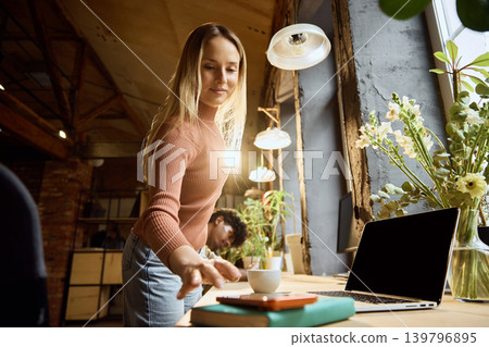 Woman reaching for smartphone for mobile banking near laptop in creative workspace Woman reaching for smartphone for mobile banking near laptop in creative workspace 139796895
