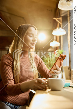 Woman checking online banking app on smartphone with coffee at workspace. Woman checking online banking app on smartphone with coffee at workspace. 139796925