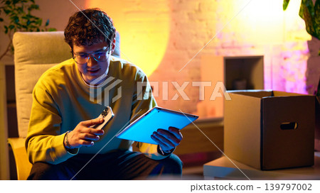 Man comparing smartphone and tablet after unboxing tech devices at home Man comparing smartphone and tablet after unboxing tech devices at home 139797002