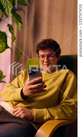 Young man using smartphone on sofa at home warm light digital shopping lifestyle Young man using smartphone on sofa at home warm light digital shopping lifestyle 139797458