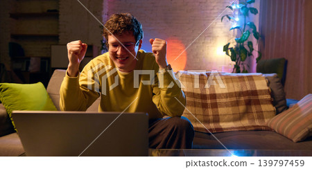 Excited customer reacting to laptop on sofa at home colorful light online shopping success 139797459