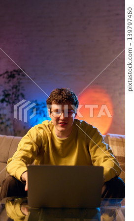 Young man using laptop on sofa at home cozy interior colorful light online shopping Young man using laptop on sofa at home cozy interior colorful light online shopping 139797460