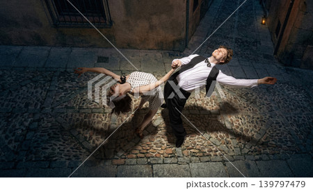 Lindy hop couple performing dip on cobblestone street at night under spotlight vintage energy Lindy hop couple performing dip on cobblestone street at night under spotlight vintage energy 139797479
