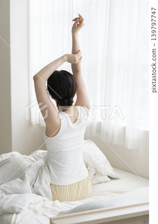 A young woman's back as she gets up and stretches in bed. 139797747