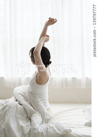 A young woman wakes up and stretches in bed. 139797777