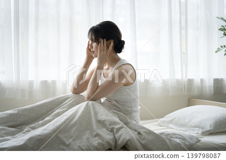 A young woman sitting on a bed, holding her head in her hands. A young woman sitting on a bed, holding her head in her hands. 139798087