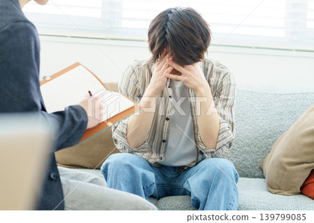 一位年輕的日本男子坐在沙發上接受心理諮商。 一位年輕的日本男子坐在沙發上接受心理諮商。 139799085