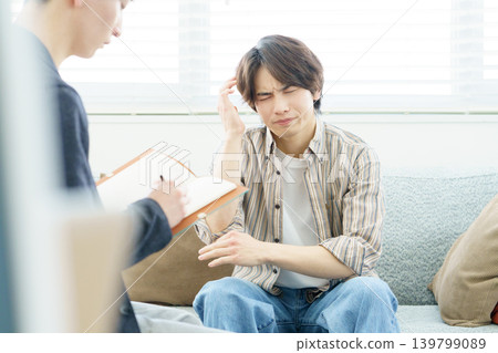 A young Japanese man sits on a sofa receiving counseling. 139799089