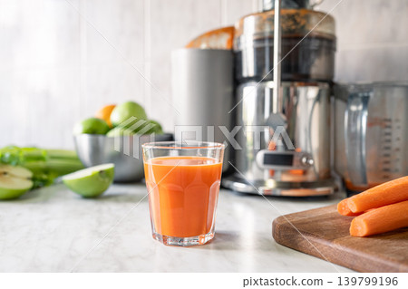Fresh carrot juice near juicer with apples and vegetables in kitchen Fresh carrot juice near juicer with apples and vegetables in kitchen 139799196