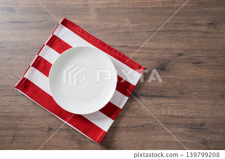 Empty white plate on red striped napkin over wooden table Empty white plate on red striped napkin over wooden table 139799208