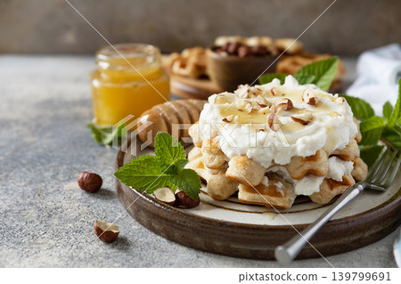 Belgian waffles with ricotta cheese, honey and hazelnuts for breakfast on a stone background. Sweet breakfast gluten free. Summer homemade recipe. Copy space. Belgian waffles with ricotta cheese, honey and hazelnuts for breakfast on a stone background. Sweet breakfast gluten free. Summer homemade recipe. Copy space. 139799691