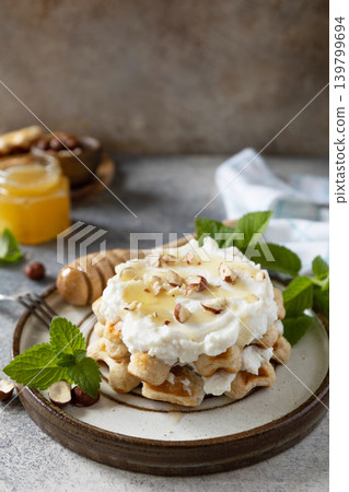 Belgian waffles with ricotta cheese, honey and hazelnuts for breakfast on a stone background. Sweet breakfast gluten free. Summer homemade recipe. Copy space. Belgian waffles with ricotta cheese, honey and hazelnuts for breakfast on a stone background. Sweet breakfast gluten free. Summer homemade recipe. Copy space. 139799694