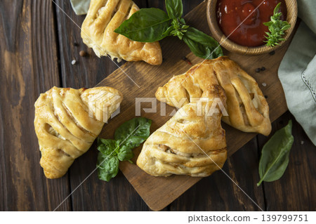Mini savory meat pies from flaky dough on a wooden board over wooden background. View from above. 139799751