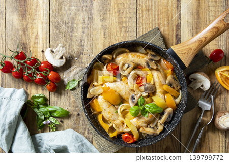 Stew of mushrooms and smoked sausages with vegetables in a frying pan on a wooden rustic table. View from above. Copy space. Stew of mushrooms and smoked sausages with vegetables in a frying pan on a wooden rustic table. View from above. Copy space. 139799772