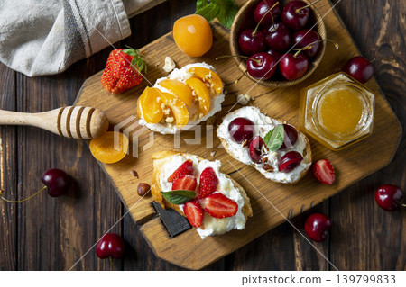 Assorted bruschetta with ricotta, honey, cherries, apricot and strawberry on a rustic table. Berries toast summer breakfast, healthy food. View from above. Copy space. 139799833