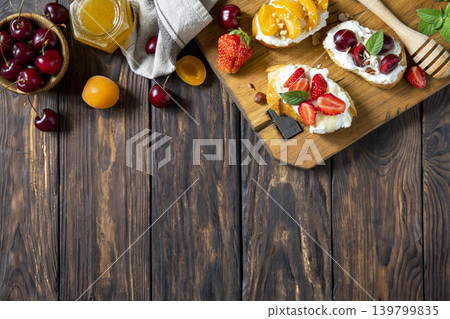 Assorted bruschetta with ricotta, honey, cherries, apricot and strawberry on a rustic table. Berries toast summer breakfast, healthy food. View from above. Copy space. 139799835