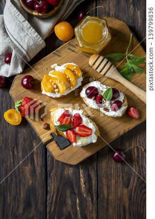 Assorted bruschetta with ricotta, honey, cherries, apricot and strawberry on a rustic table. Berries toast summer breakfast, healthy food. View from above. Copy space. 139799836