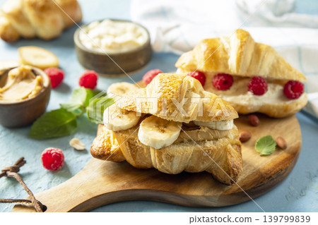 French pastry close up, freshly baked croissants with peanut butter, raspberries and banana on a blue stone background. Healthy food dessert concept. 139799839