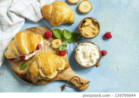 French pastry, freshly baked croissants with peanut butter, raspberries and banana on a blue stone background. Healthy food dessert concept. View from above. Copy space. 139799844