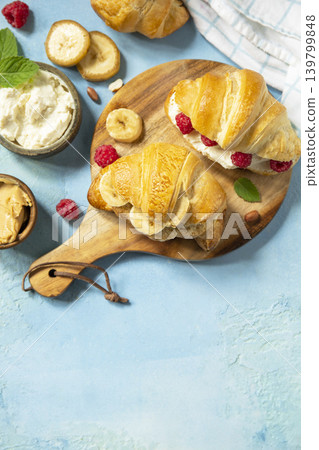 French pastry, freshly baked croissants with peanut butter, raspberries and banana on a blue stone background. Healthy food dessert concept. View from above. Copy space. 139799848