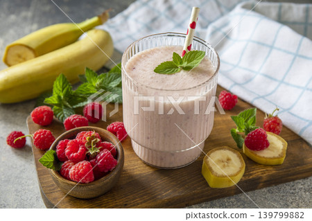 Pink raspberries and banana fruit smoothie or milk protein shake on stone tabletop. Yogurt cocktail, natural detox. Liquid ice cream. Pink raspberries and banana fruit smoothie or milk protein shake on stone tabletop. Yogurt cocktail, natural detox. Liquid ice cream. 139799882