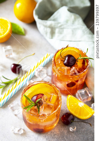 Refreshing summer cherry and orange cocktail cola lemonade or mojito cocktail in glass with ice and mint on stone tabletop. Refreshing summer cherry and orange cocktail cola lemonade or mojito cocktail in glass with ice and mint on stone tabletop. 139799897