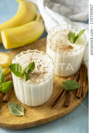 Vegan banana smoothies with cinnamon in drinking glass on a blue stone background. Detox menu, refreshing summer drink. Vegan banana smoothies with cinnamon in drinking glass on a blue stone background. Detox menu, refreshing summer drink. 139799907