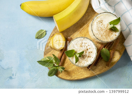 Vegan banana smoothie with cinnamon in drinking glass on a blue stone background. Detox menu, refreshing summer drink. View from above. Copy space. Vegan banana smoothie with cinnamon in drinking glass on a blue stone background. Detox menu, refreshing summer drink. View from above. Copy space. 139799912