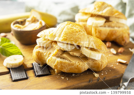 French pastry close up, freshly baked croissants with peanut butter and banana on a grey stone background. Healthy food dessert concept. French pastry close up, freshly baked croissants with peanut butter and banana on a grey stone background. Healthy food dessert concept. 139799938