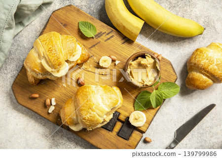 French pastry, freshly baked croissants with peanut butter and banana on a grey stone background. Healthy food dessert concept. View from above. French pastry, freshly baked croissants with peanut butter and banana on a grey stone background. Healthy food dessert concept. View from above. 139799986