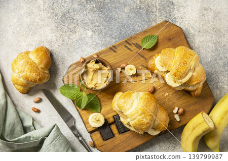 French pastry, freshly baked croissants with peanut butter and banana on a grey stone background. Healthy food dessert concept. View from above. French pastry, freshly baked croissants with peanut butter and banana on a grey stone background. Healthy food dessert concept. View from above. 139799987