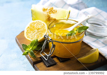 Sweet melon and citrus jam, homemade jelly preserves in small glass jar with fresh melon slices on a blue stone tabletop. Homemade preserve. Copy space. Sweet melon and citrus jam, homemade jelly preserves in small glass jar with fresh melon slices on a blue stone tabletop. Homemade preserve. Copy space. 139799992