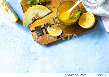 Sweet melon and citrus jam, homemade jelly preserves in small glass jar with fresh melon slices on a blue stone tabletop. Homemade preserve. View from above. Copy space. Sweet melon and citrus jam, homemade jelly preserves in small glass jar with fresh melon slices on a blue stone tabletop. Homemade preserve. View from above. Copy space. 139799997