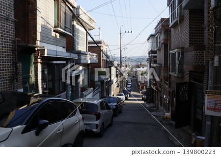 Narrow Urban Street with Residential Buildings and Parked Cars 139800223